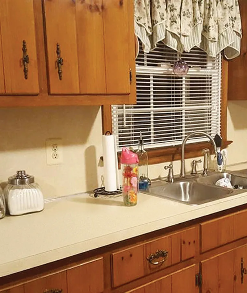 Old kitchen countertop with wooden cabinets, double sink, and various containers labeled before renovation.