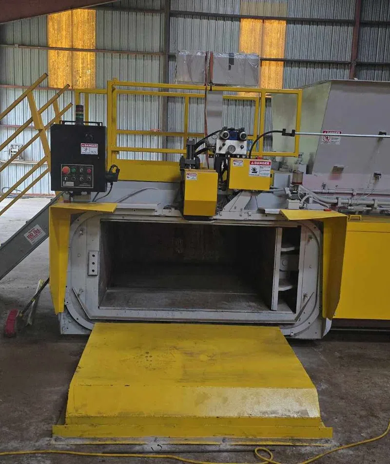 Industrial yellow waste compactor machine inside a warehouse with safety railings and control panel.