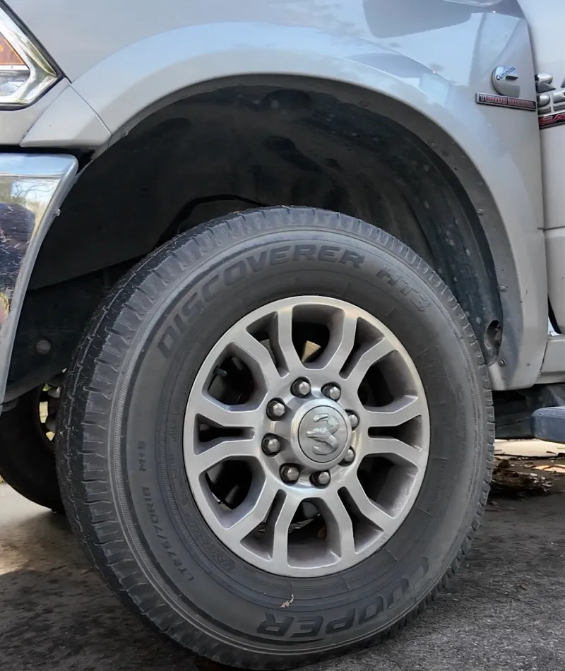 Close-up of a Cooper Discoverer AT3 tire mounted on a silver Dodge truck wheel on concrete ground.
