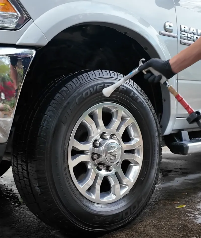 Person cleaning silver alloy wheel and tire on gray Ram 2500 truck with tire shine applicator.