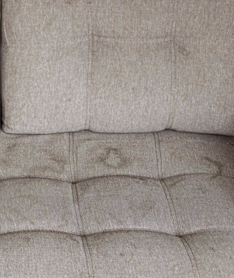 Beige fabric sofa with visible dark stains on cushioned seat and backrest upholstery.