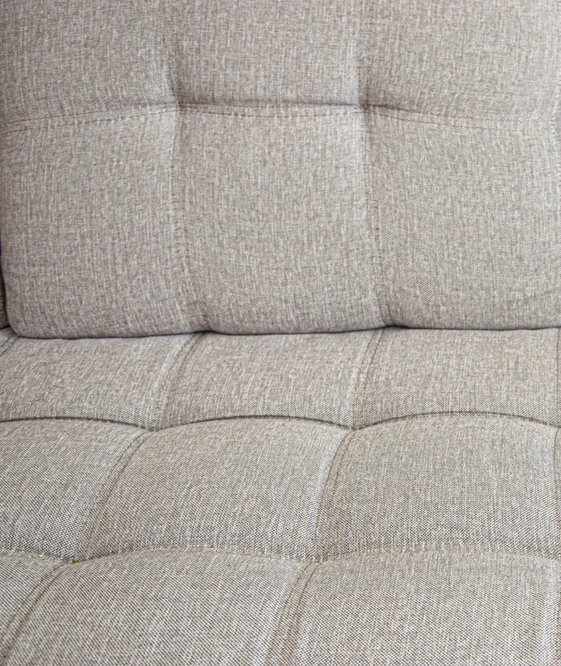 Close-up of a beige textured fabric sofa cushion with tufted square pattern stitching.