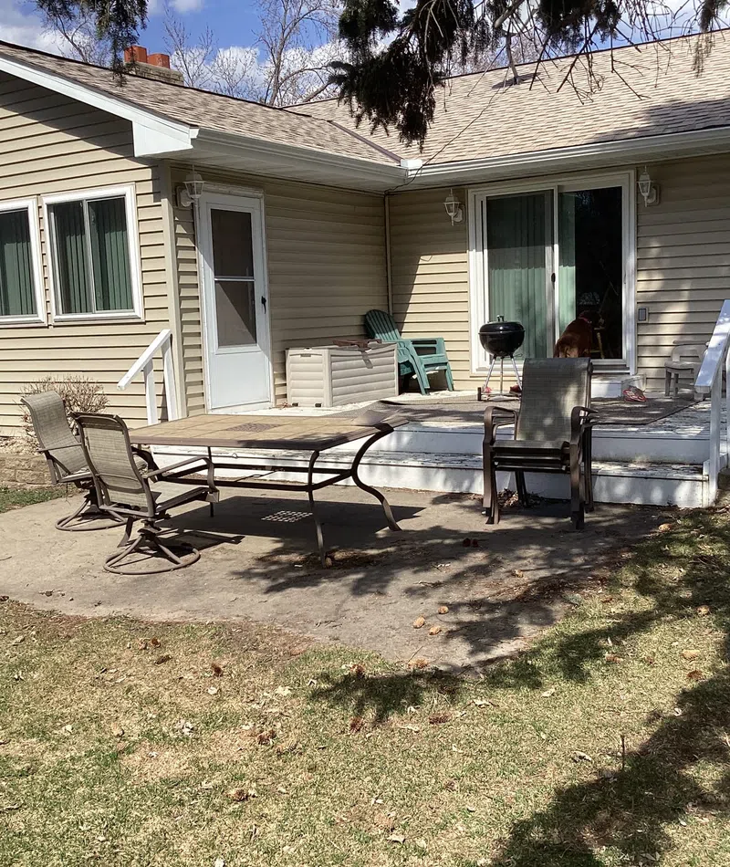 Backyard patio with outdoor table, chairs, grill, and beige siding house under a clear sky.