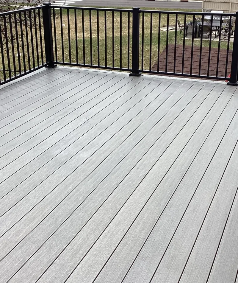 Spacious gray composite deck with black metal railing overlooking a suburban backyard and trees in early spring.