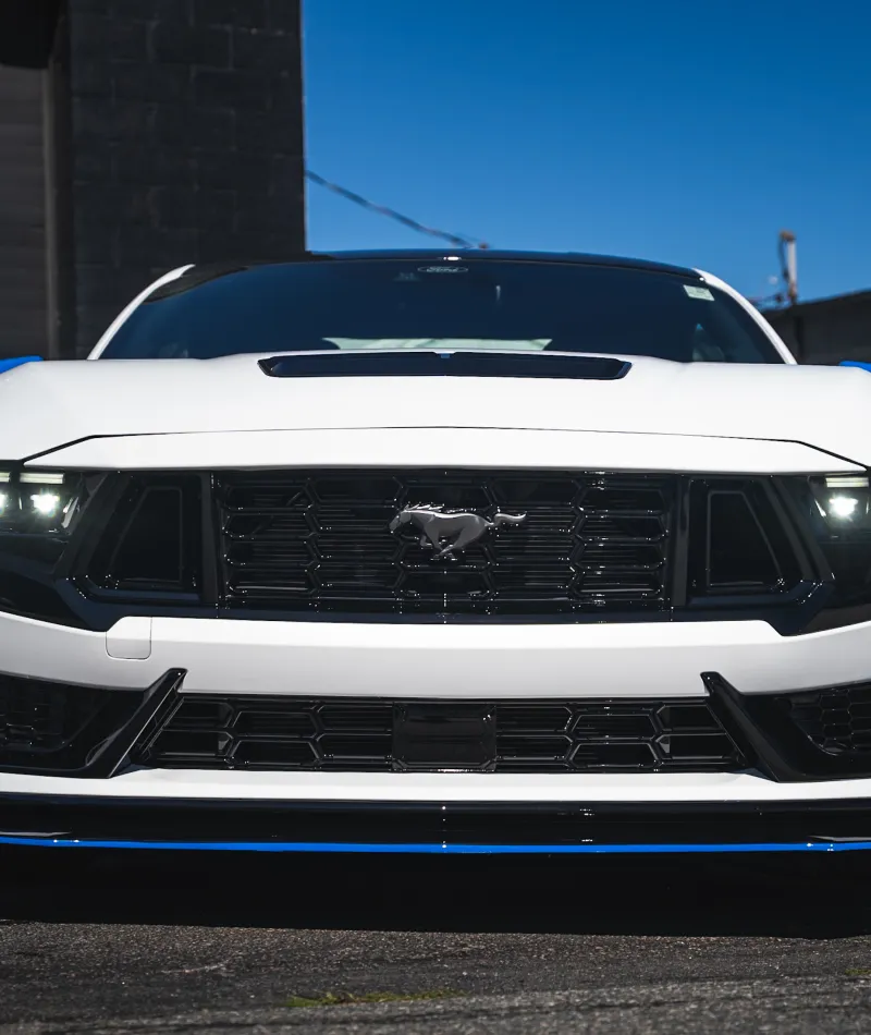 Front view of a white Ford Mustang with LED headlights and black grille under clear blue sky.