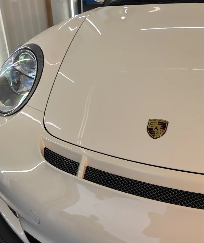 Close-up of a white Porsche sports car hood and headlight with emblem in a garage setting