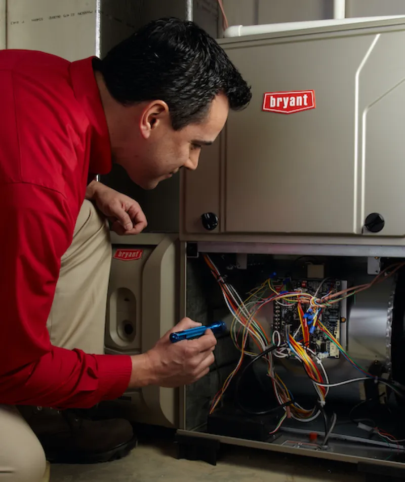 Technician examining the wiring of a Bryant furnace in a basement setting.