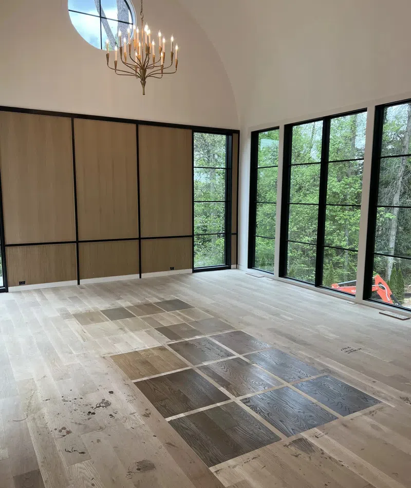 Spacious room with large windows, chandelier, wooden flooring samples displayed on light hardwood floor.