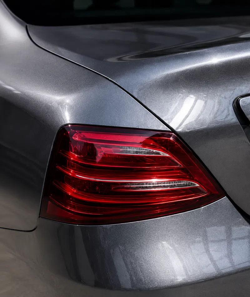 Close-up of a metallic gray car's rear with prominent red taillight and smooth body curves under light reflection.