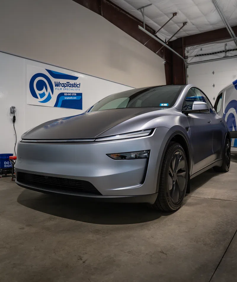 Sleek silver electric SUV parked in an indoor garage next to a WrapTastic film specialists sign.
