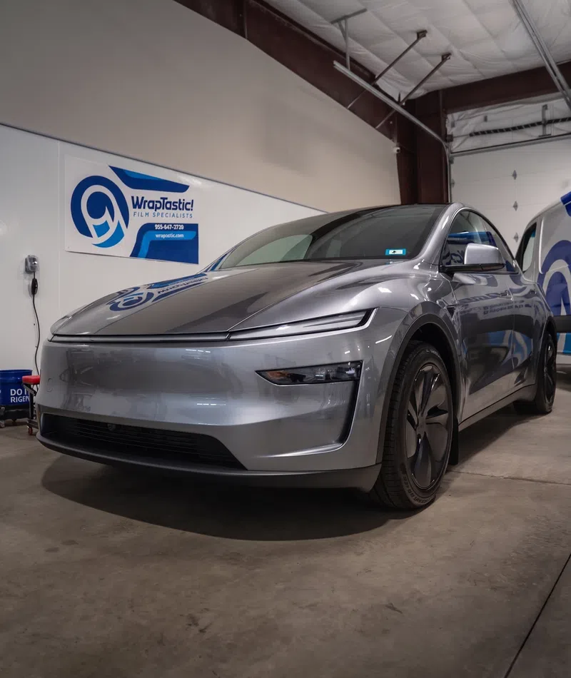 Sleek silver electric car parked inside an industrial garage with WrapTastic signage on the wall.