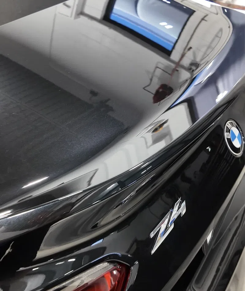 Close-up of black BMW Z4 rear with shiny surface, taillight, and clear reflections of surroundings.