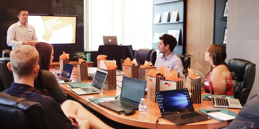 a group of people sitting around a table with laptops
