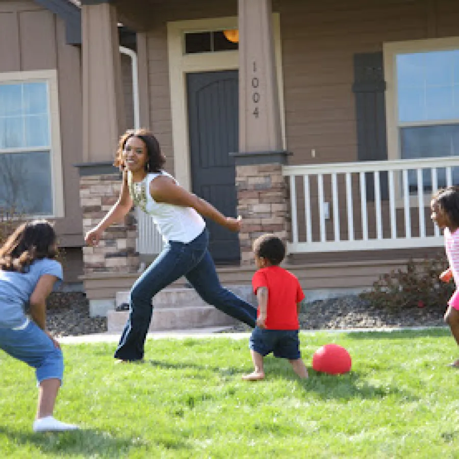 A woman playing with children on a lawn in front of a house, enjoying outdoor fun and games.
