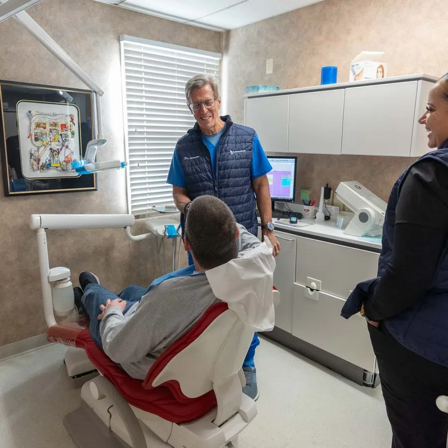 Dentist and assistant interacting with patient in a modern dental clinic with equipment and cabinetry.