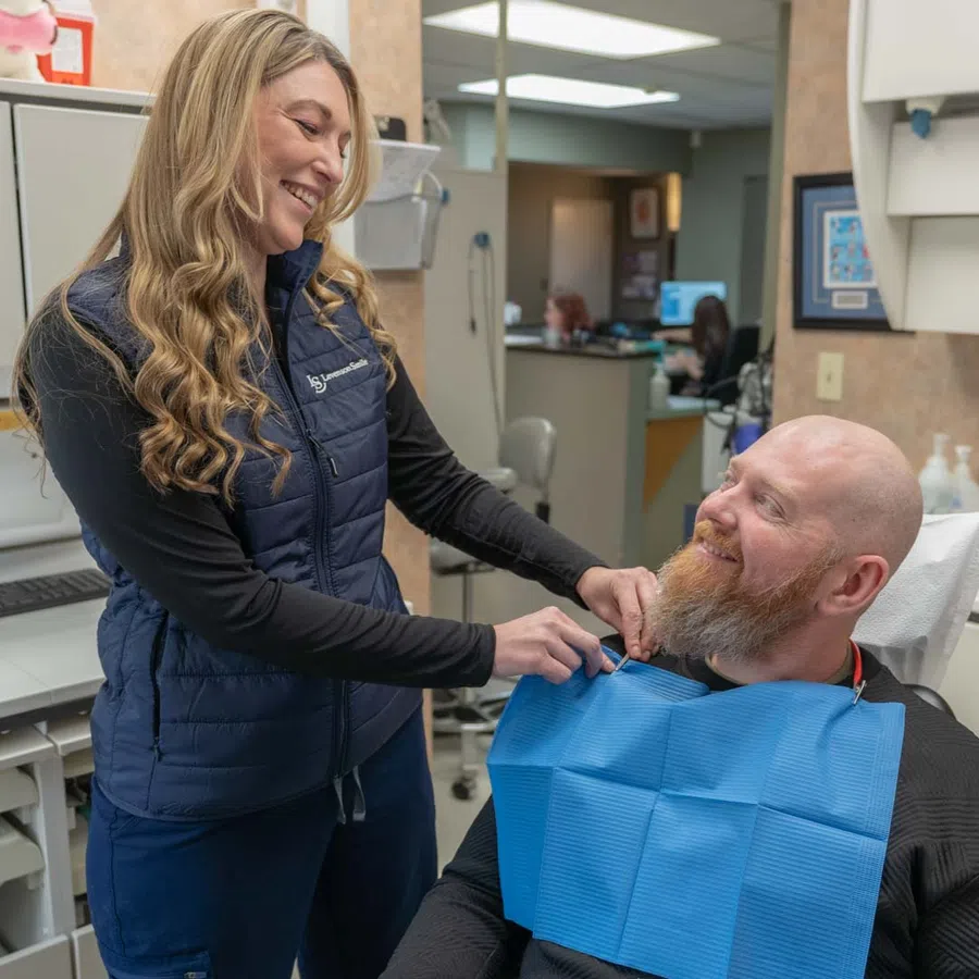 Dental hygienist smiling while preparing a male patient for a dental checkup in a clinic room