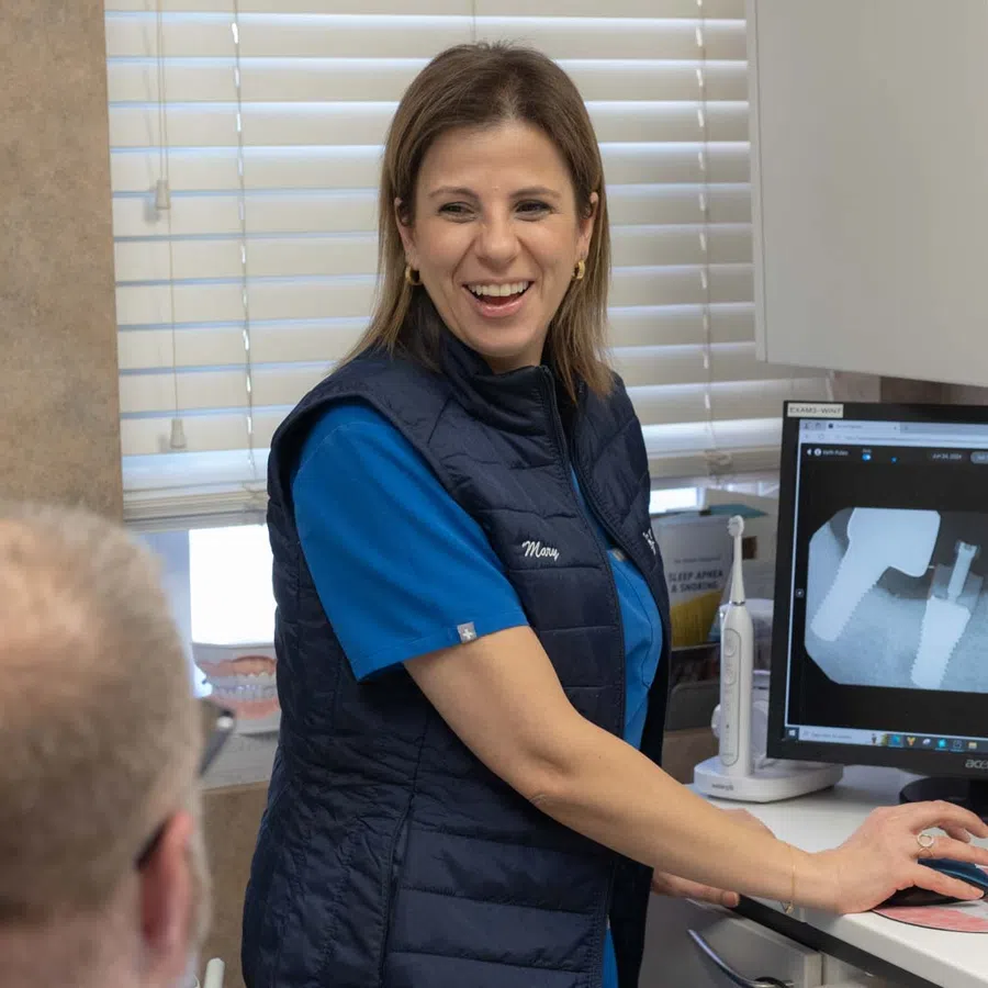 Dental professional showing patient a tooth X-ray on a computer screen during consultation.