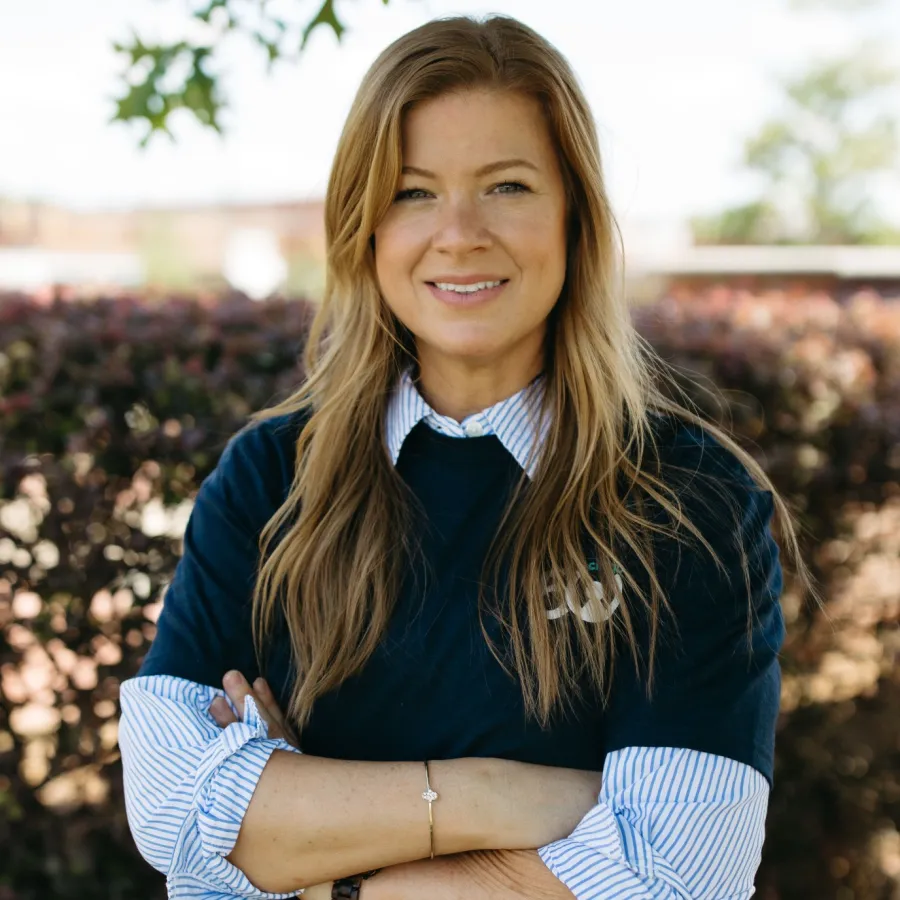 Confident woman with long hair in casual attire standing outdoors with arms crossed.