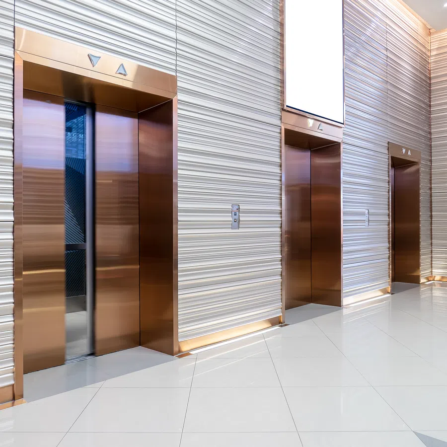 Modern elevator bank with four bronze doors and textured white walls in a bright, clean lobby.