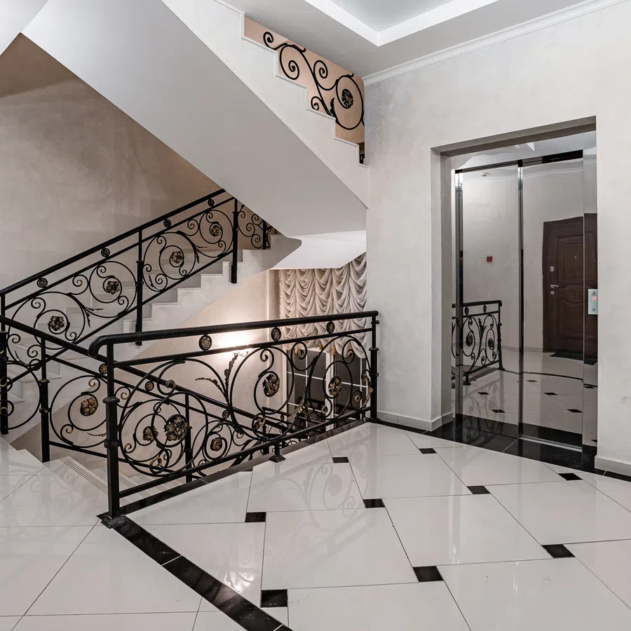 Modern stairwell interior with ornate black wrought iron railings and polished white tiled floors.