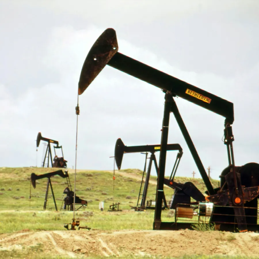 Multiple oil pumpjacks operating on a grassy plain under a cloudy sky during daytime.