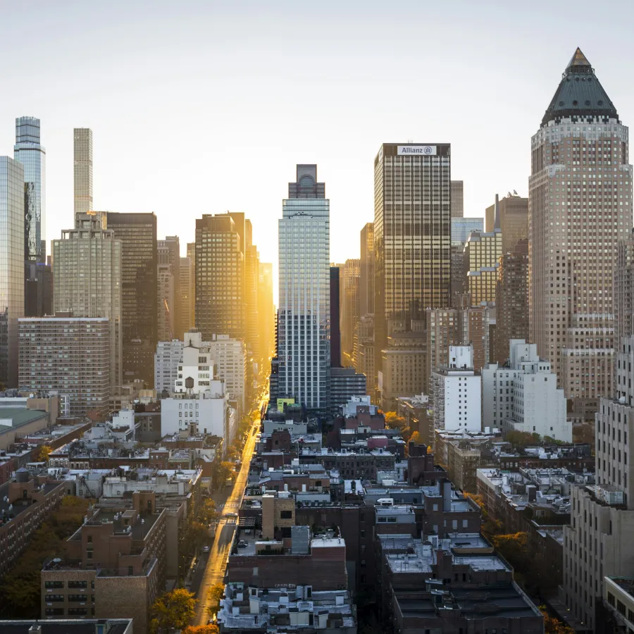 Sunset over a dense urban cityscape with tall skyscrapers and a glowing street cutting through the buildings.