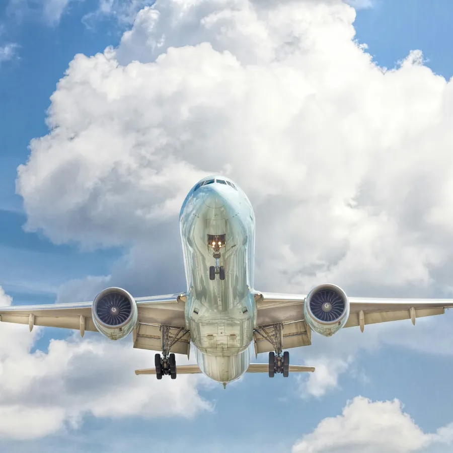 Commercial airplane flying low against a blue sky with white clouds, showing landing gear deployed.