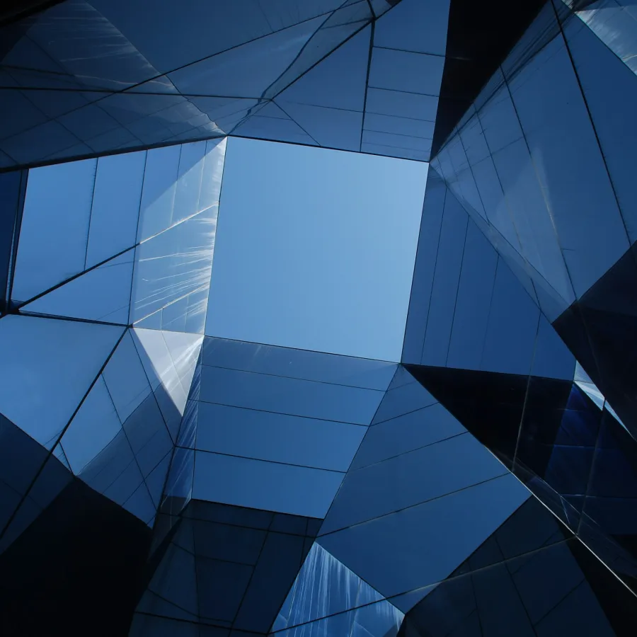 Abstract blue glass building facade with geometric reflections and clear sky visible through the center opening
