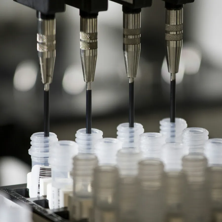 Four precision pipettes dispensing liquid into multiple clear plastic laboratory tubes in a science lab.