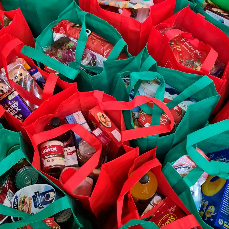 Red and green reusable grocery bags filled with assorted food items and drinks packed closely together.
