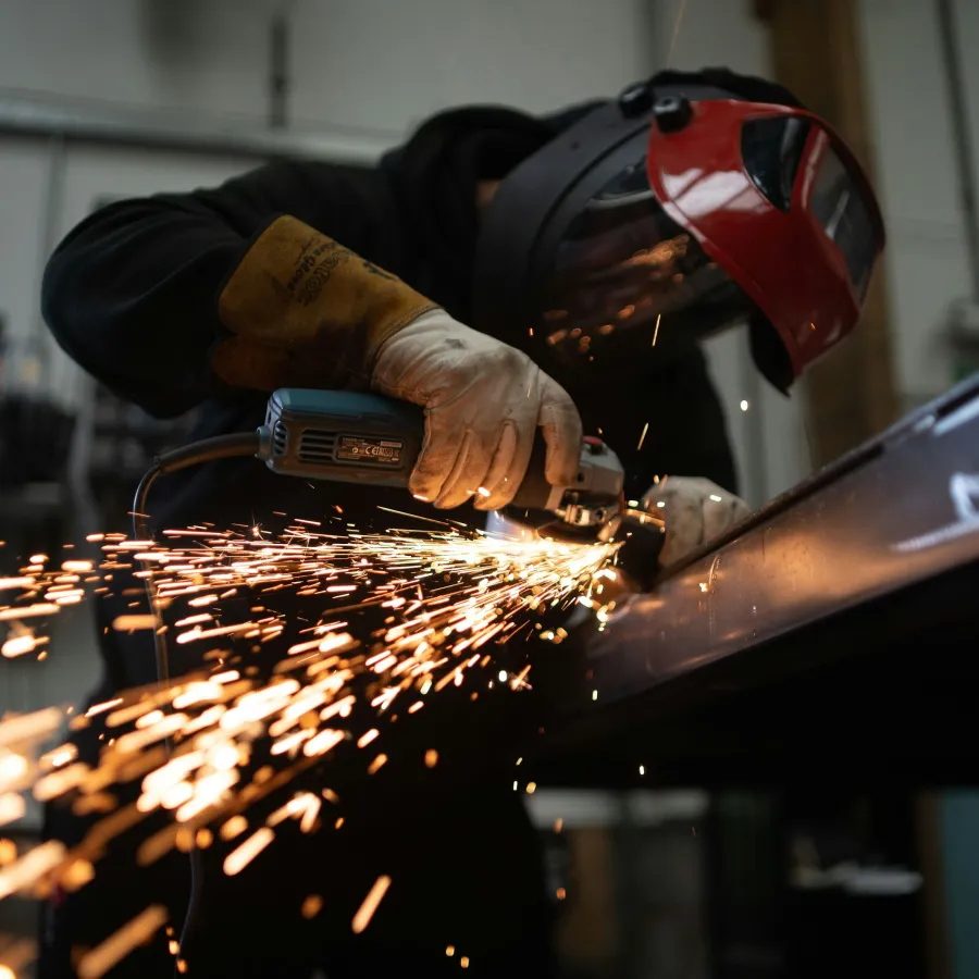 Worker using angle grinder on metal with sparks flying in a workshop wearing protective gear.