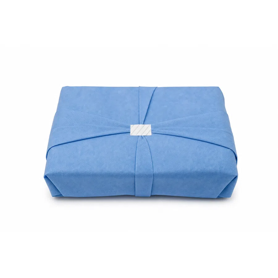 Rectangular blue gift wrapped in fabric with a white tag on a white background.