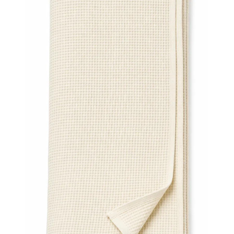 Folded beige waffle weave cotton blanket with a corner slightly turned over on white background