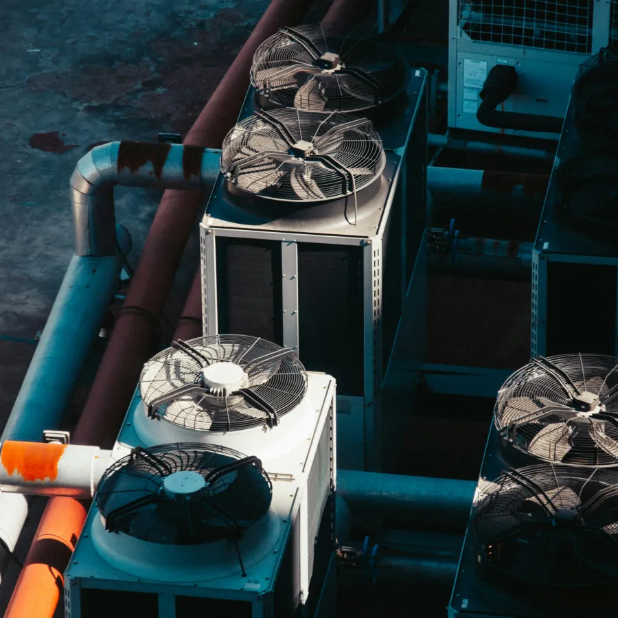 Industrial HVAC units with metal fans and pipes on rooftop casting shadows in daylight.