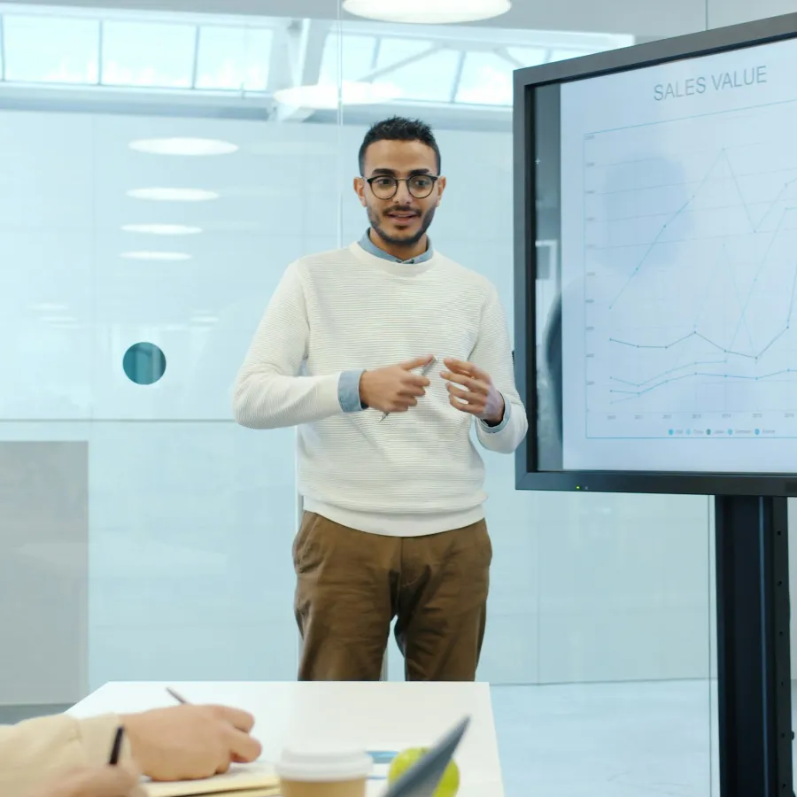 Man giving sales presentation with graphs on screen in modern office setting