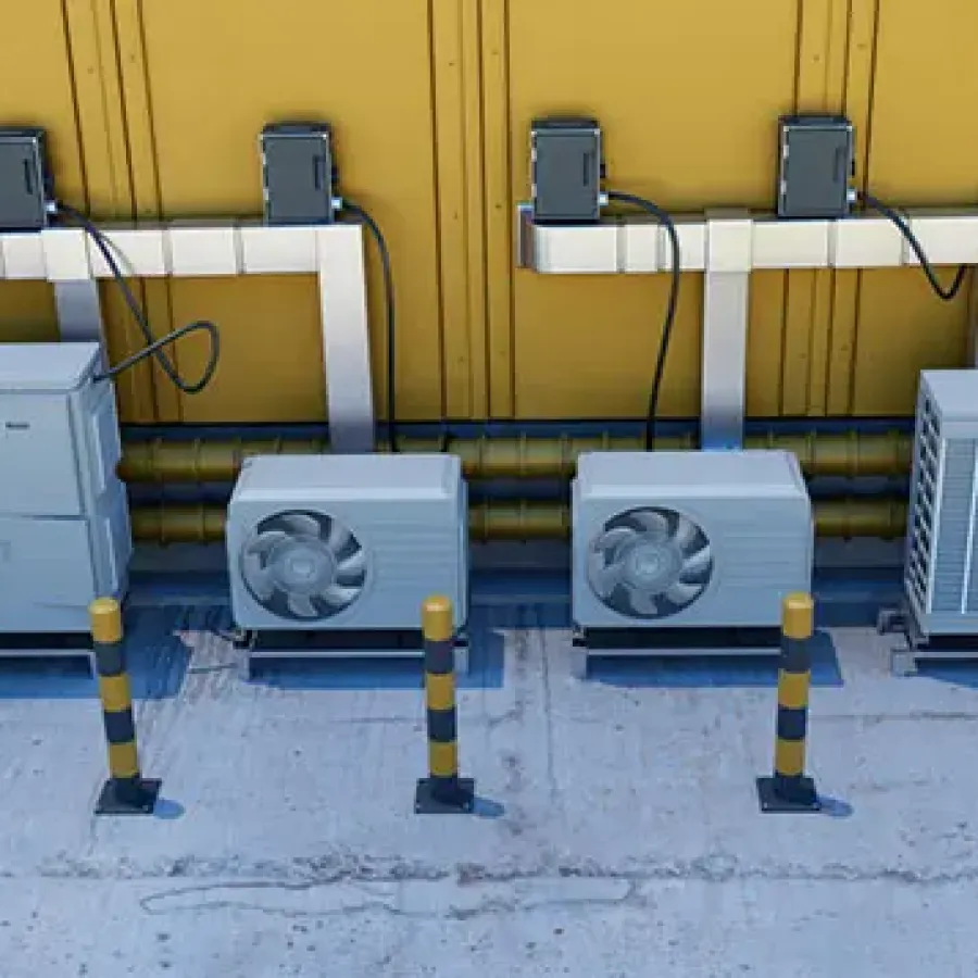 Row of industrial air conditioning units with protective bollards in front against a yellow wall.
