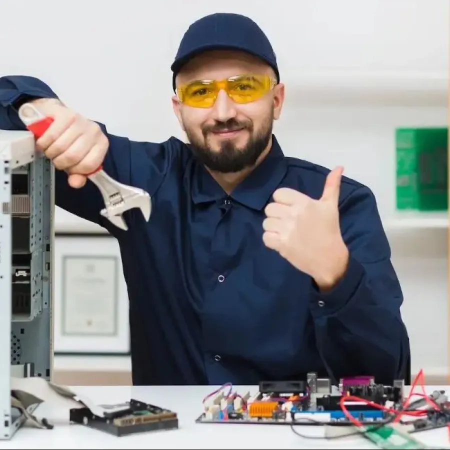 Technician in safety glasses repairing computer hardware with thumbs up gesture at desk