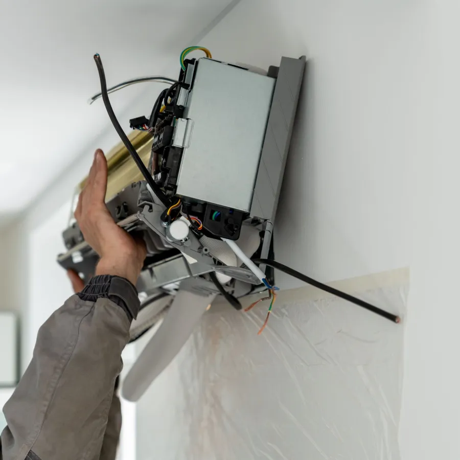 Technician installing or repairing a wall-mounted air conditioning unit with exposed wires and components indoors