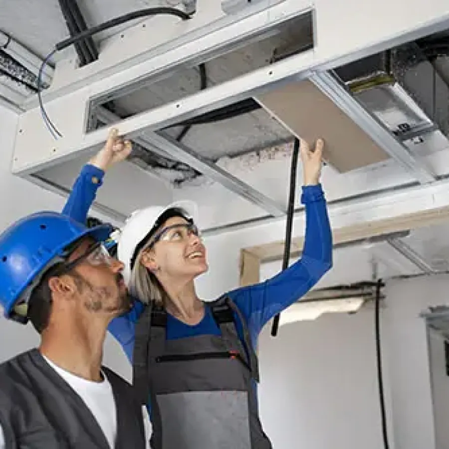 Two construction workers in helmets installing or inspecting a ceiling panel in an unfinished building interior
