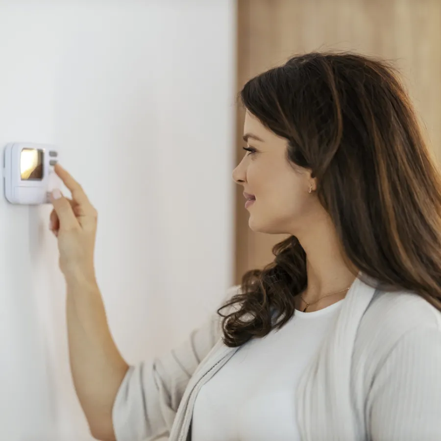 Woman adjusting a digital thermostat on the wall in a modern home interior setting