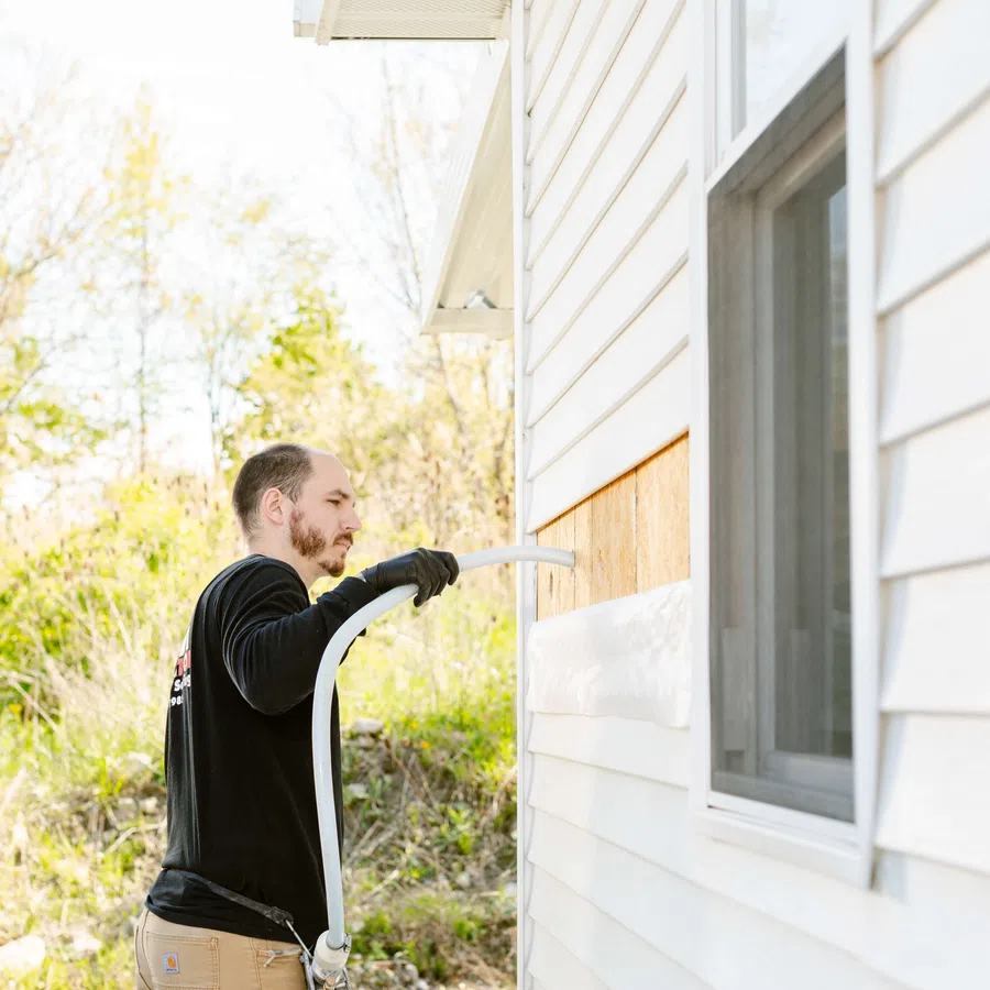 Man installing insulation foam into a wall cavity of a white house during home improvement.