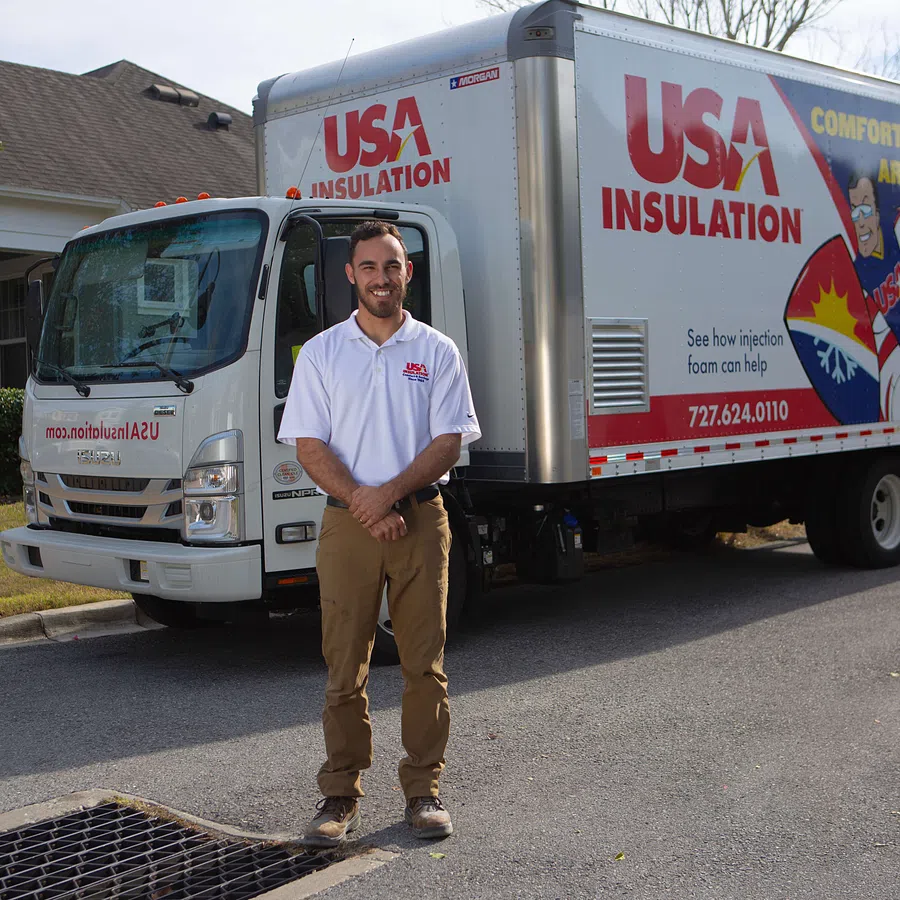 Man in USA Insulation shirt standing in front of a branded insulation service truck on a residential street.