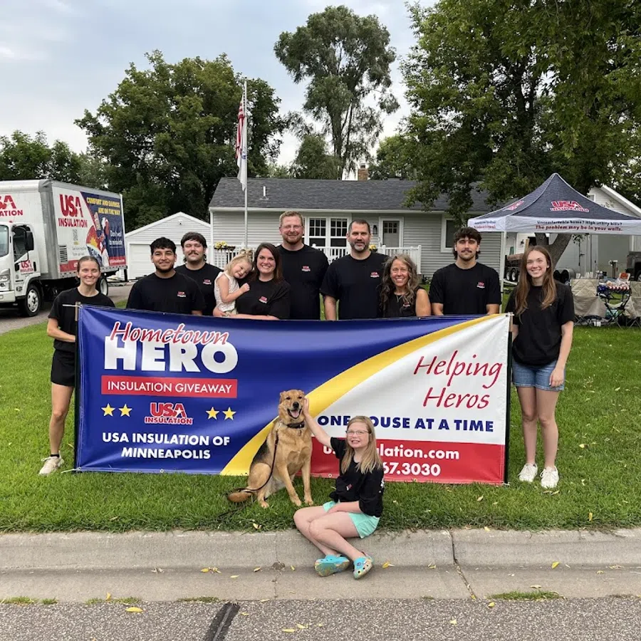 Group of people holding Hometown Hero insulation giveaway banner with dog and child in front on a suburban lawn.