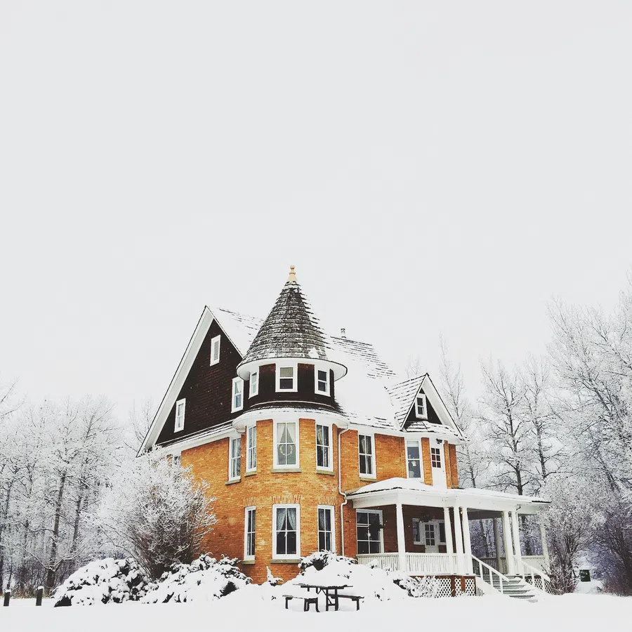 Victorian-style brick house with snow-covered roof and yard surrounded by frosted trees in winter.