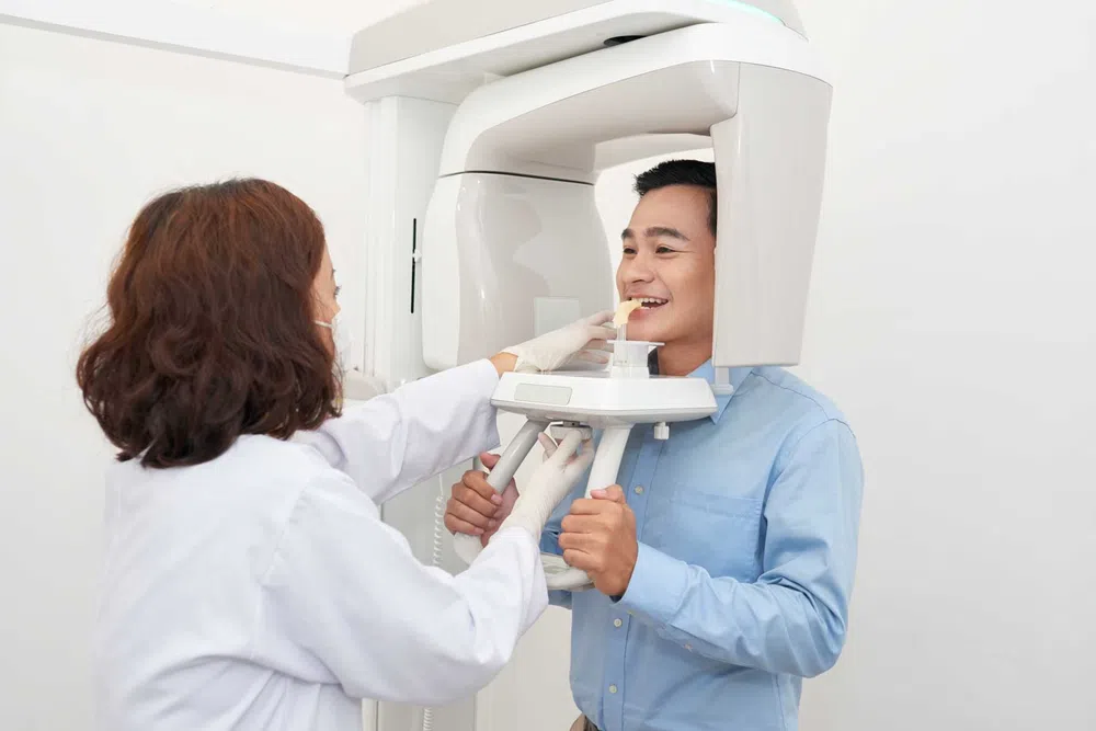 Bright modern dental clinic with dental chair, monitor, sink, and white cabinetry under natural light.