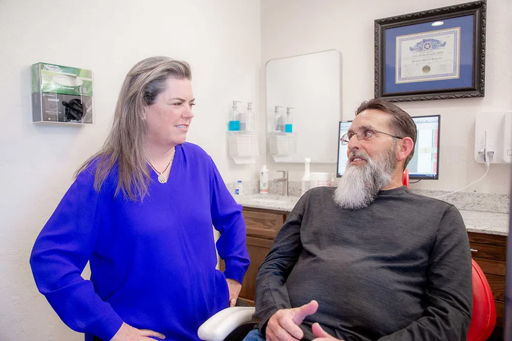 Female healthcare professional in blue blouse consulting male patient with gray beard in medical office