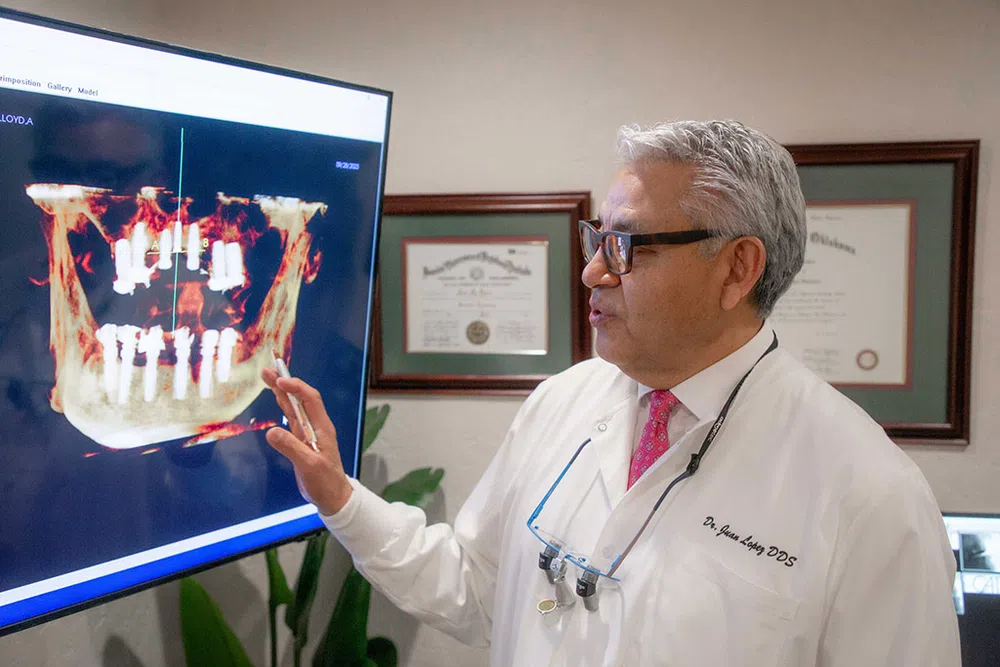 Dentist examining 3D digital X-ray of dental implants on a large screen in his office.