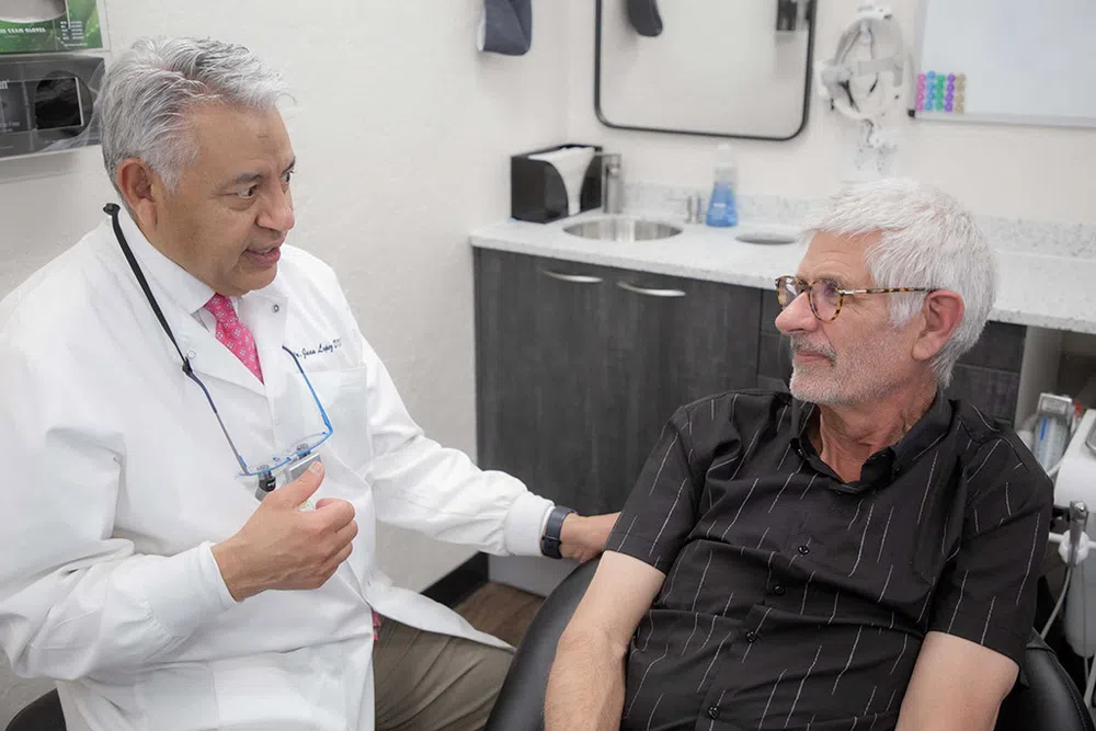Doctor in white coat consulting and reassuring elderly male patient in a medical office setting.