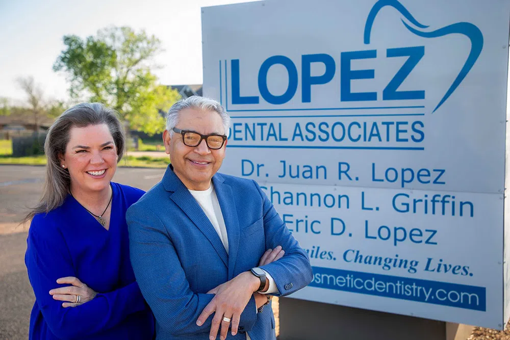 Smiling dental professionals standing in front of Lopez Dental Associates outdoor sign on sunny day