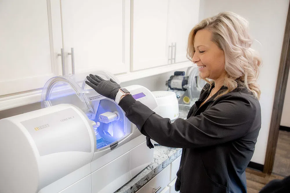Woman operating a dental milling machine in a modern dental lab, wearing black gloves and a smartwatch.